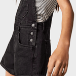 Woman wearing black denim dungaree shorts with adjustable straps
