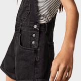 Woman wearing black denim dungaree shorts with adjustable straps