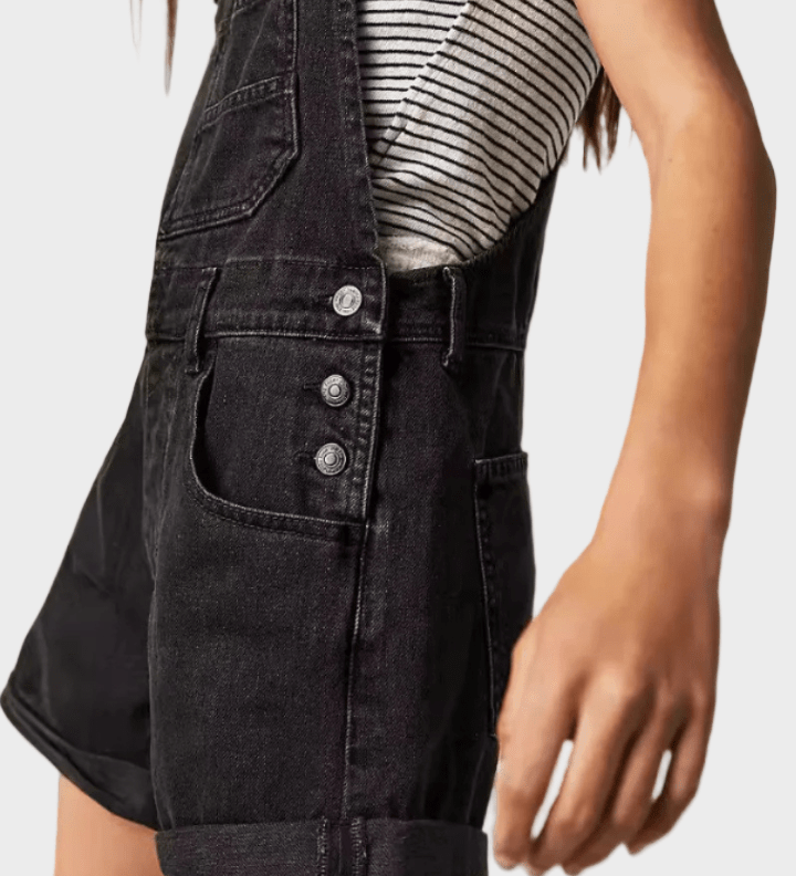 Woman wearing black denim dungaree shorts with adjustable straps